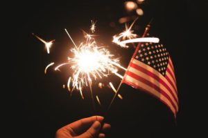 hand holding sparkler and mini flag of the US